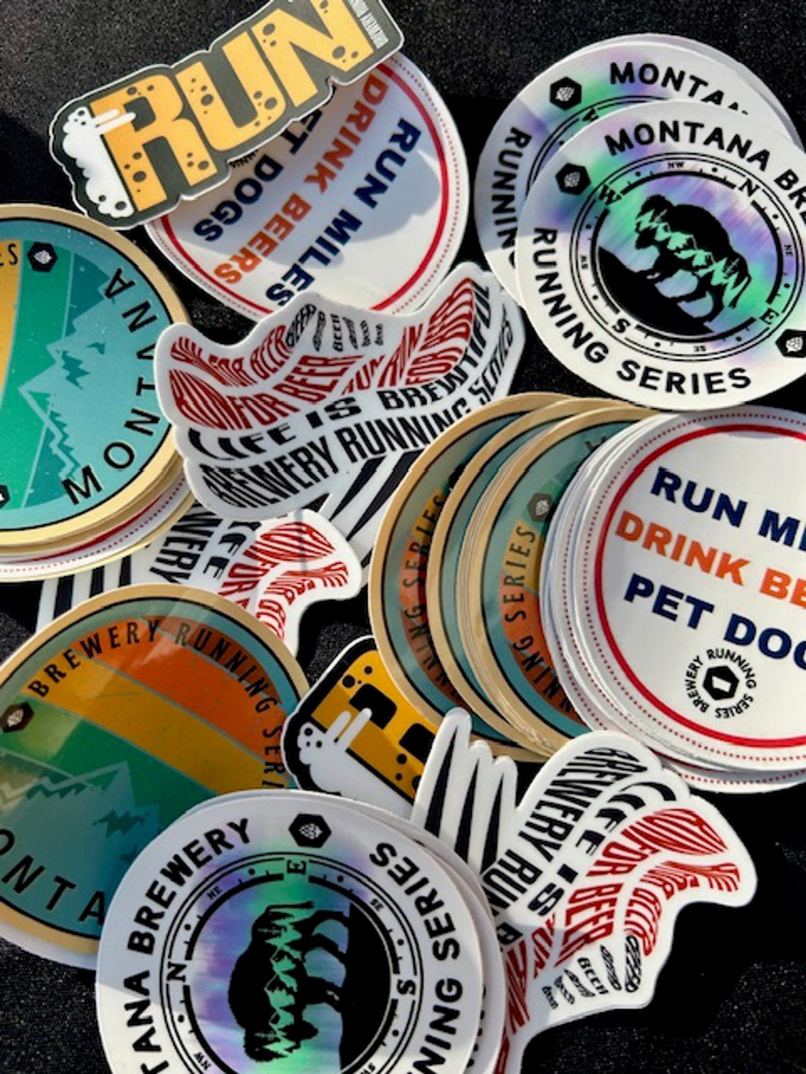 A scattered collection of colorful round and die-cut stickers, featuring phrases like βRUN,β βRUN MORE DRINK BEER PET DOGS,β and βMontana Brewery Running Series,β with graphic designs and logos.