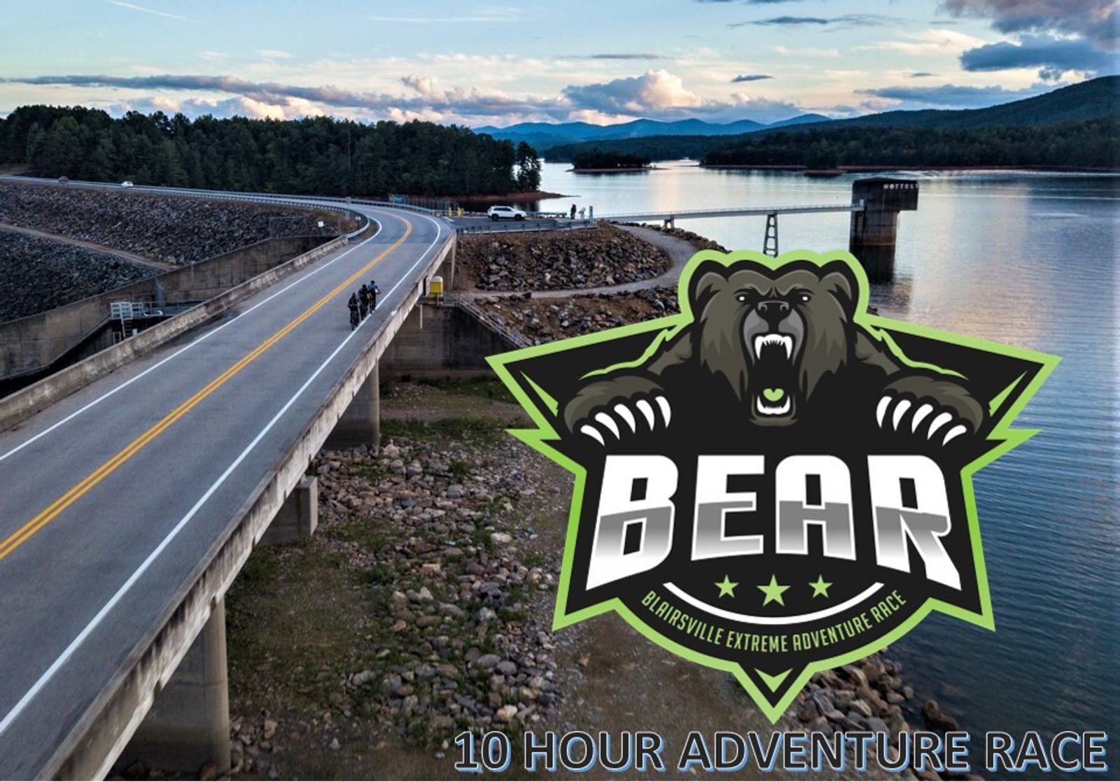 An aerial view of a road over a dam with water and mountains in the background. A large logo of a roaring bear with "BEAR" and "Blairsville Extreme Adventure Race" overlays the image. Text reads "10 Hour Adventure Race.