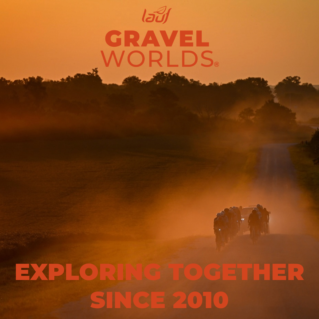 Cyclists ride on a dusty road lined with trees at sunset, casting a warm orange glow. The text "Gravel Worlds" and "Exploring Together Since 2010" is overlaid on the image.