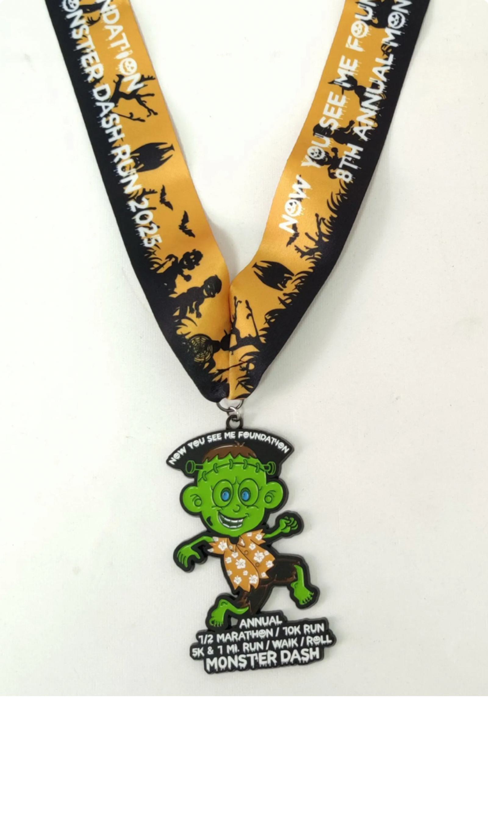 A black and orange race medal featuring a green monster in an orange polka-dot outfit. The ribbon reads “Now You See Me Foundation Monster Dash Run 2023.” The medal lists various race events.