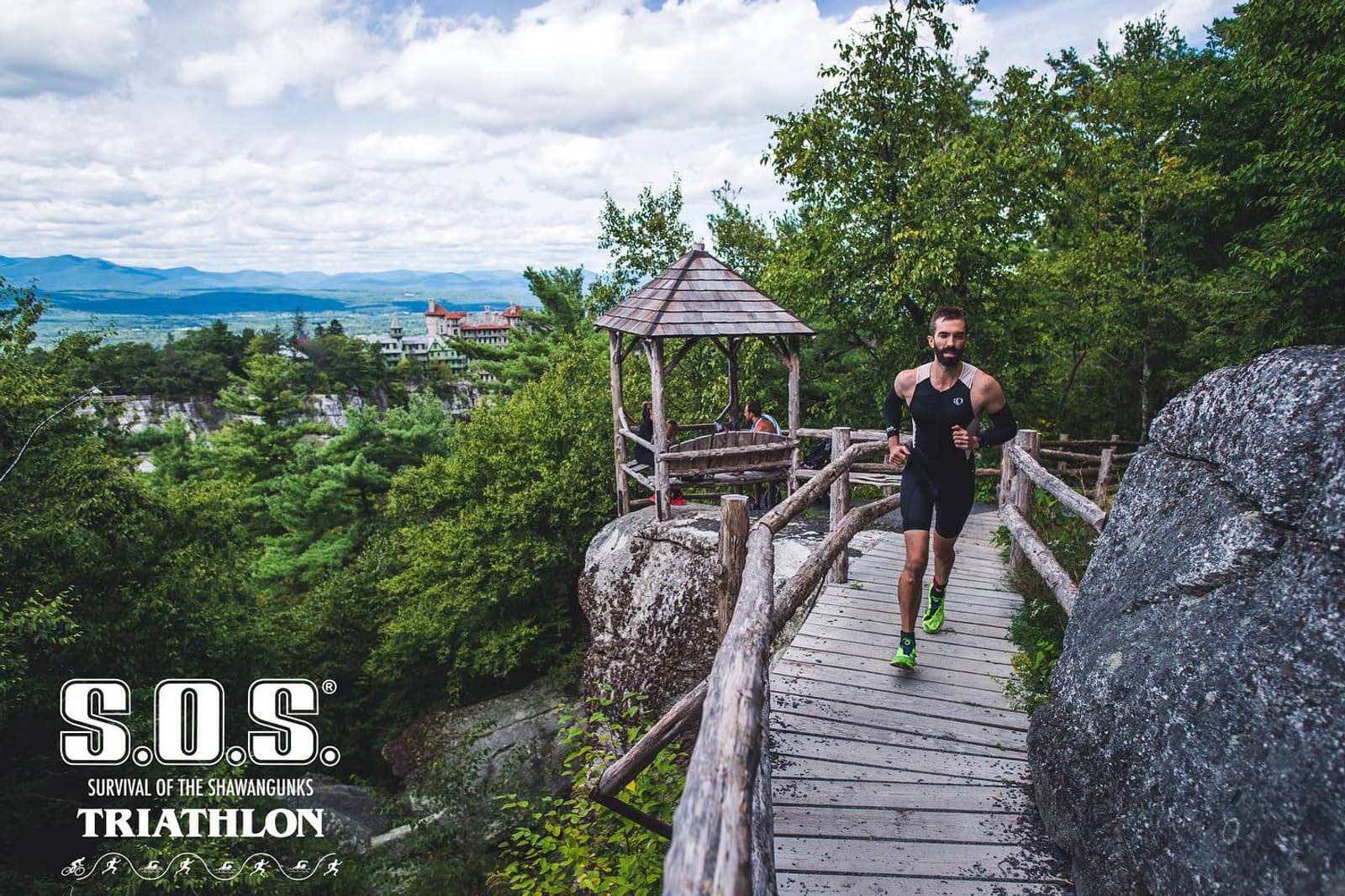 A man in athletic gear runs across a wooden bridge on a rocky, forested trail with a scenic mountain view. A gazebo and large rocks are nearby. The image features the S.O.S. Triathlon logo in the corner.