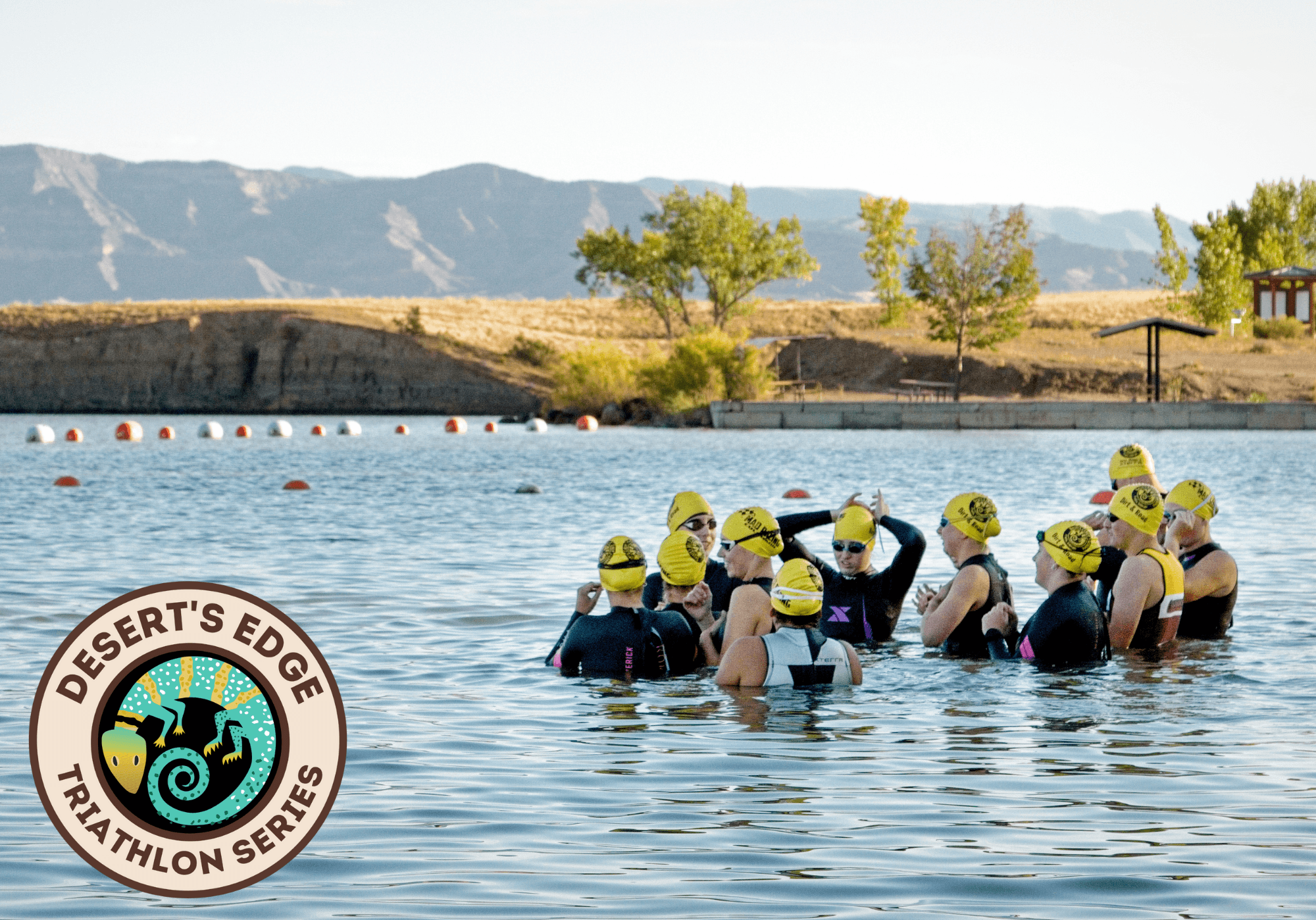 Athletes wearing yellow swim caps and wetsuits gather in a lake before a race, with mountains in the background. The Desertβs Edge Triathlon Series logo appears in the lower left corner.