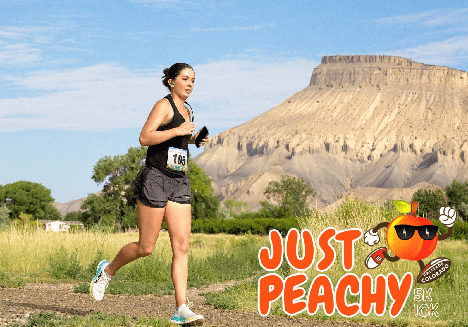 A woman in athletic wear runs outdoors near a mesa, holding a phone, with a race bib numbered 106. The "Just Peachy 5K 10K" race logo with a cartoon peach is at the bottom right corner.