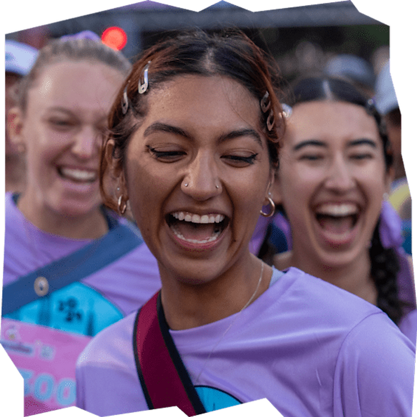 A group of young women wearing purple shirts are smiling and laughing outdoors, enjoying a lively event together.
