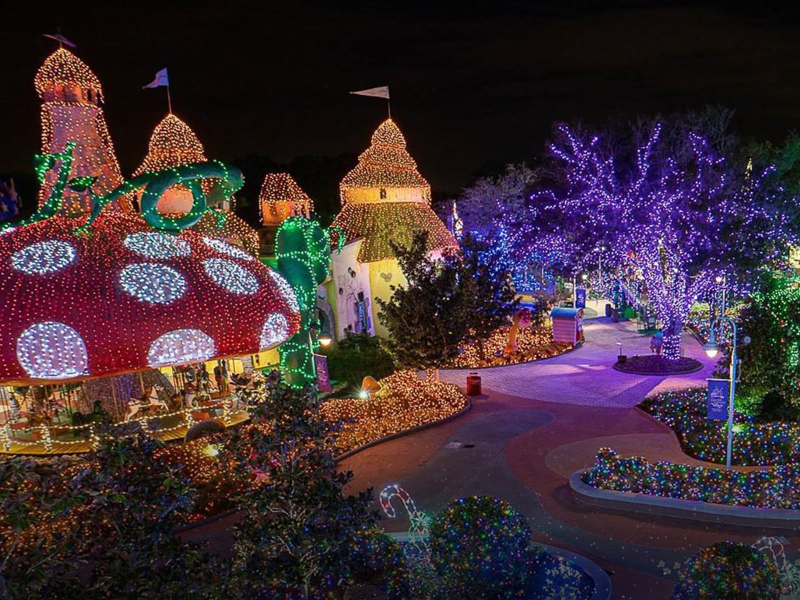 A whimsical nighttime scene featuring mushroom-shaped houses and trees decorated with colorful holiday lights, creating a vibrant, enchanting atmosphere in a garden or amusement park setting.